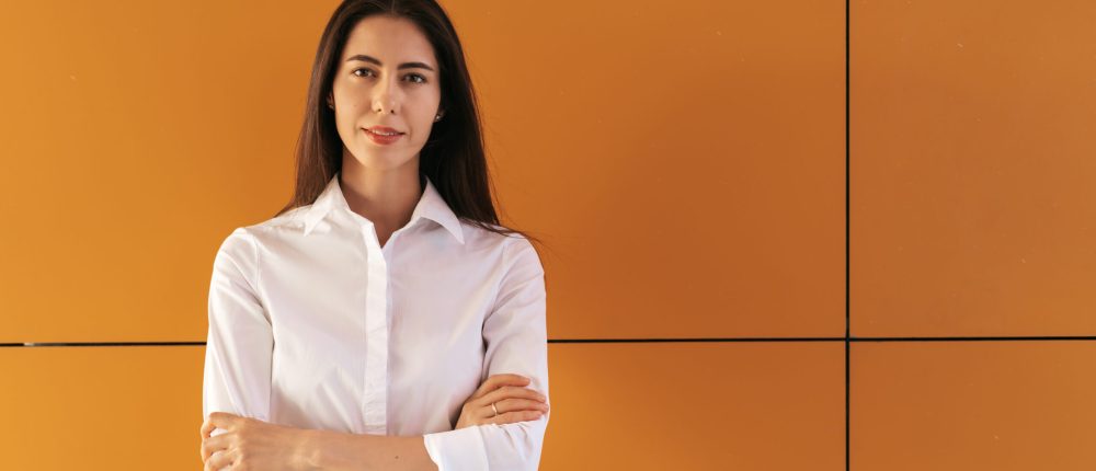 Pretty brunette woman portrait on yellow background in white shirt and hands crossed